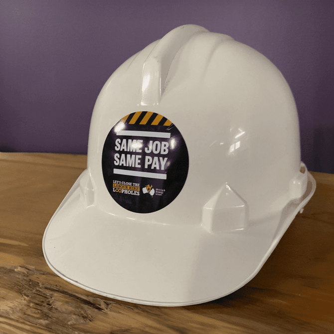 A white hard hat featuring a circular sticker. The sticker has a logo and bold text. A white hard hat featuring a circular sticker. The sticker has a logo and bold text.