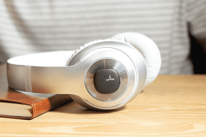 A pair of silver headphones with white ear pads resting on a wooden surface next to a book.