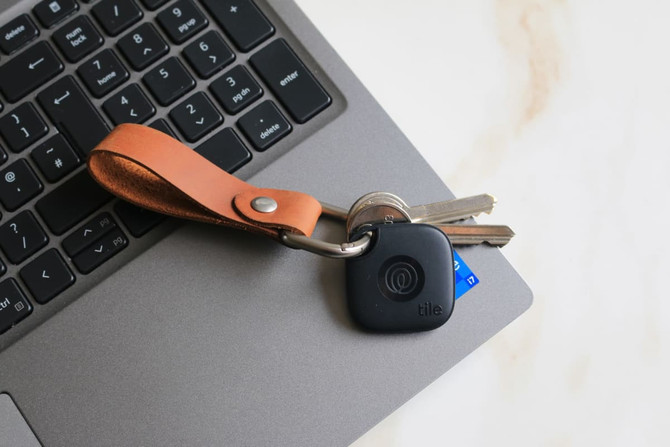 A black Tile Mate attached to a silver keyring with a genuine leather fob on a laptop keyboard.