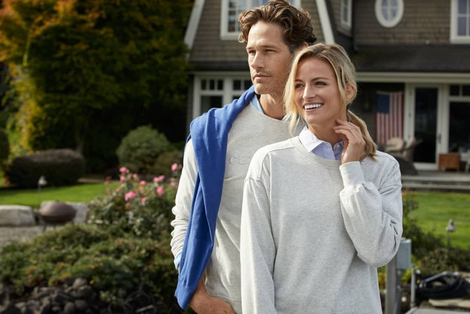 A grey crew neck sweatshirt is worn by a smiling woman outdoors, alongside a man in a blue sweatshirt. A grey crew neck sweatshirt is worn by a smiling woman outdoors, alongside a man in a blue sweatshirt.