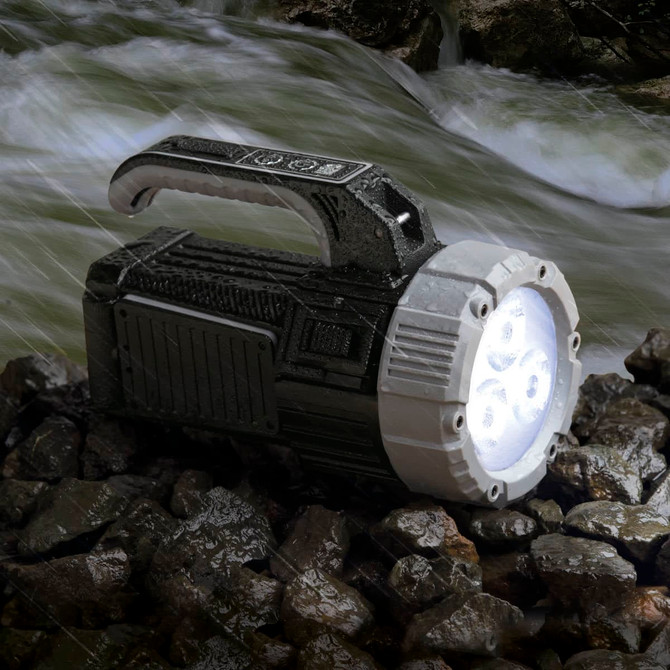 A black and silver torch rests on rocky ground, with a bright light emitting from its front, surrounded by flowing water.