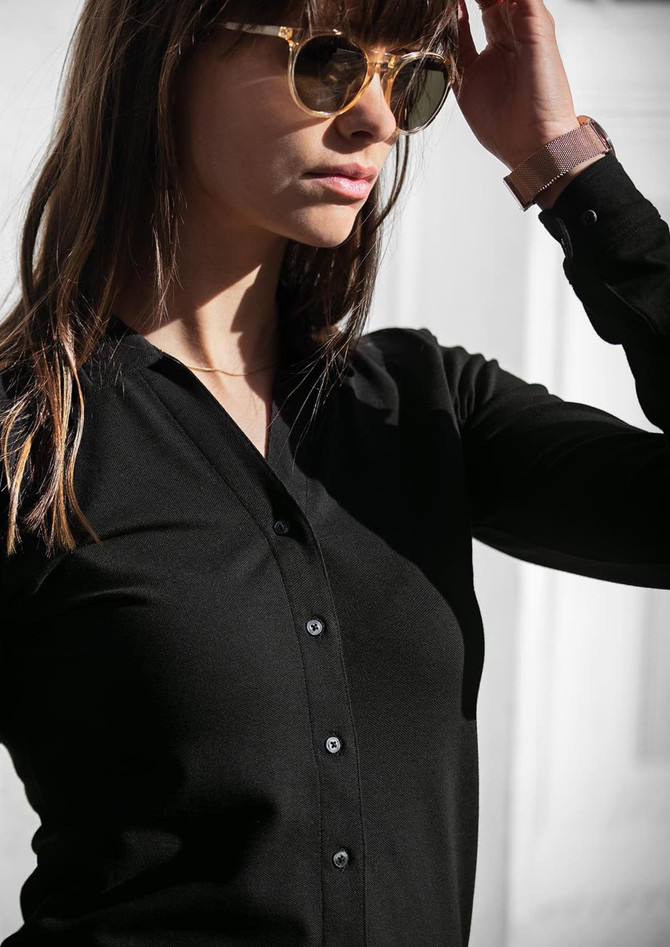 A black polo shirt is worn by a woman with sunglasses, featuring a buttoned front and long sleeves.