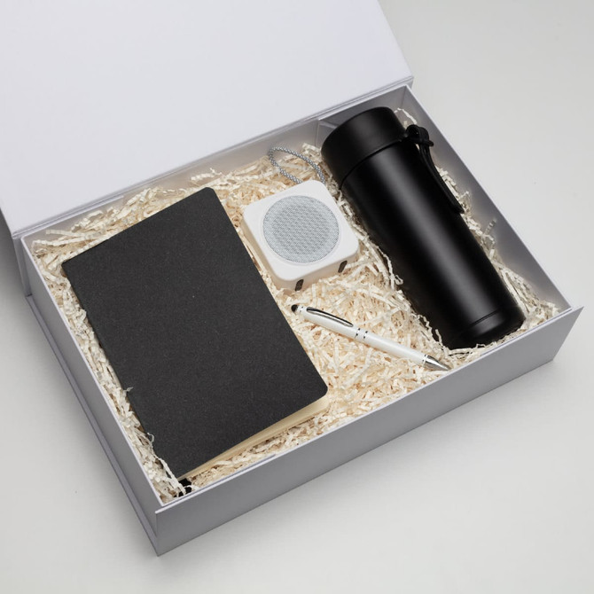 A black notebook, a white speaker, a black drink bottle, and a pen in a gift box with shredded paper.