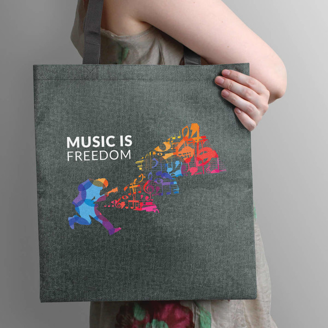 A person holding a grey tote bag featuring a colourful music-themed graphic and a branding logo.