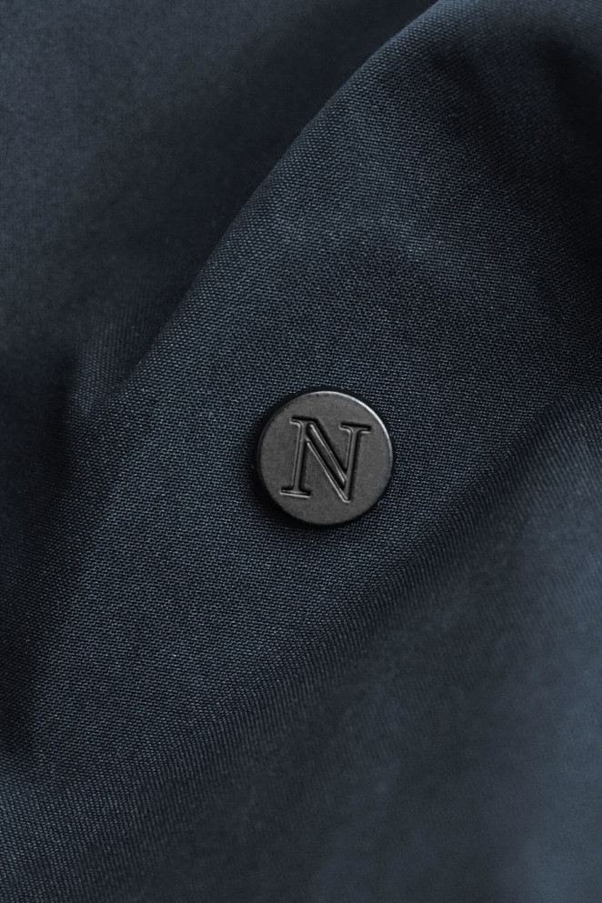 A close-up of a dark navy fabric with a round black logo badge embossed with the letter "N".