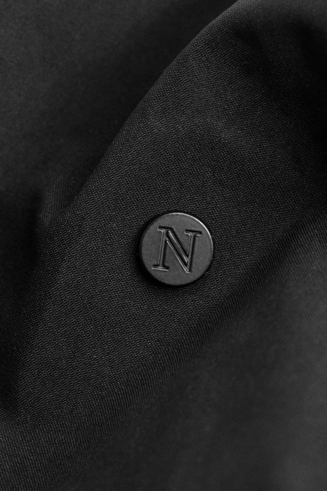 A close-up of a black fabric featuring a round black logo with an embossed letter 'N'.