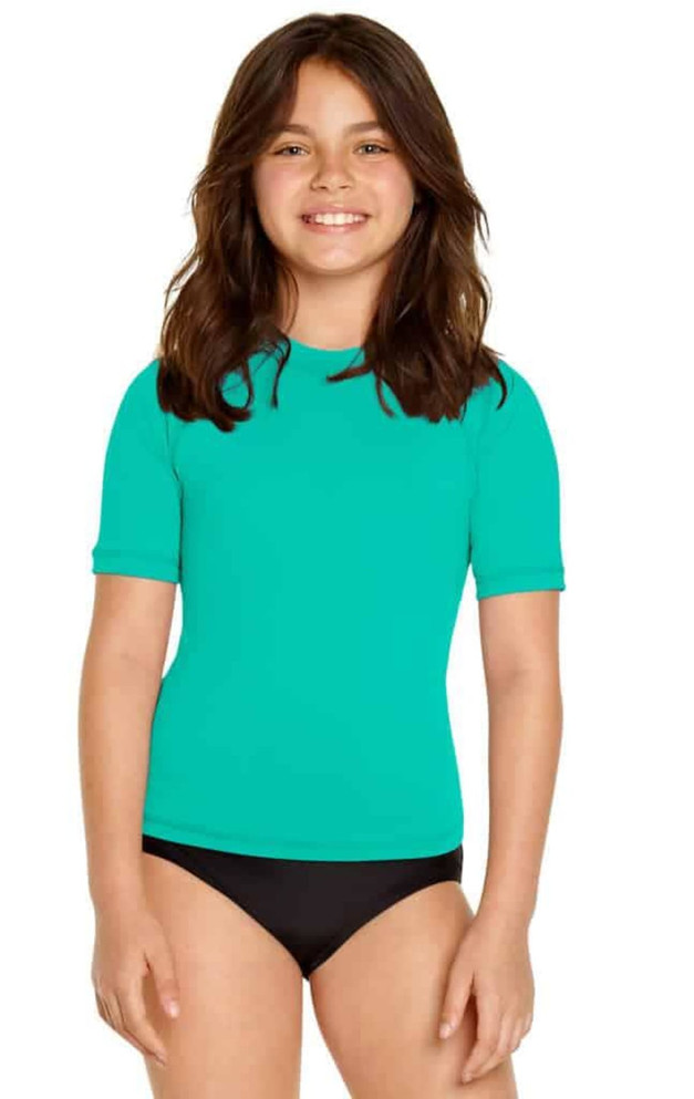 A youth short sleeve rashie in bright turquoise, featuring a logo, worn with black swim bottoms.