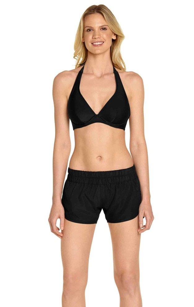 A woman in a black bikini top and black swim shorts, featuring a waistband and a simple design.