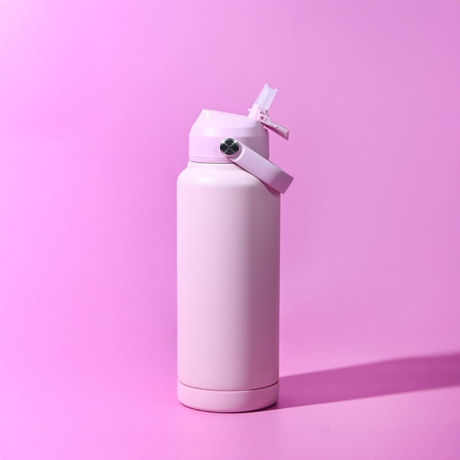 A drink bottle in a soft pink colour with a flip-top lid and a strap. It features a logo on the side.
