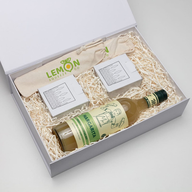 A drink bottle and two packaged items in a white gift box filled with shredded paper, featuring a logo.