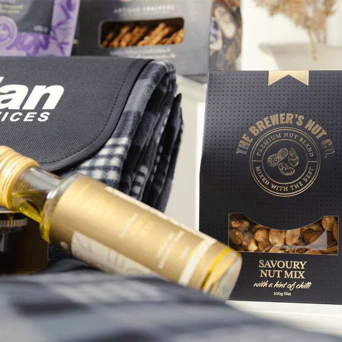 A drink bottle, a picnic blanket, and a Savoury Nut Mix packaged in a black box. The blanket features a checkered pattern.