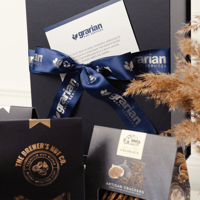 A gourmet picnic gift pack featuring artisan crackers, gourmet nuts, and a decorative box with a blue ribbon and branding.