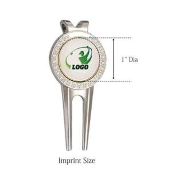 A silver golf divot tool featuring a round ball marker, with a logo in the centre and measuring 1 inch in diameter.