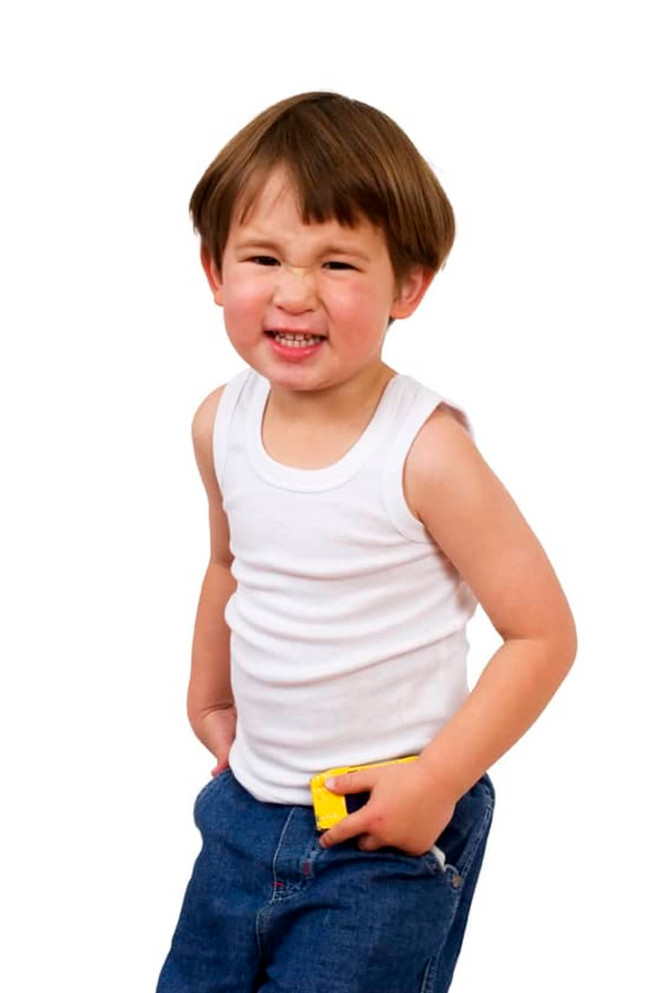 A child in a white singlet and blue jeans, smiling with hands in pockets, showcasing a playful expression.