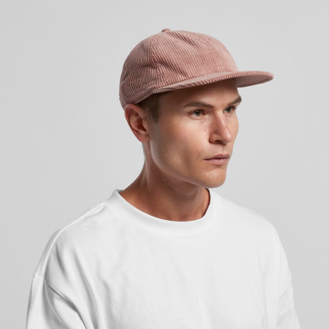 A pink cord cap held by a man wearing a white t-shirt, featuring a minimalist design and a small logo.