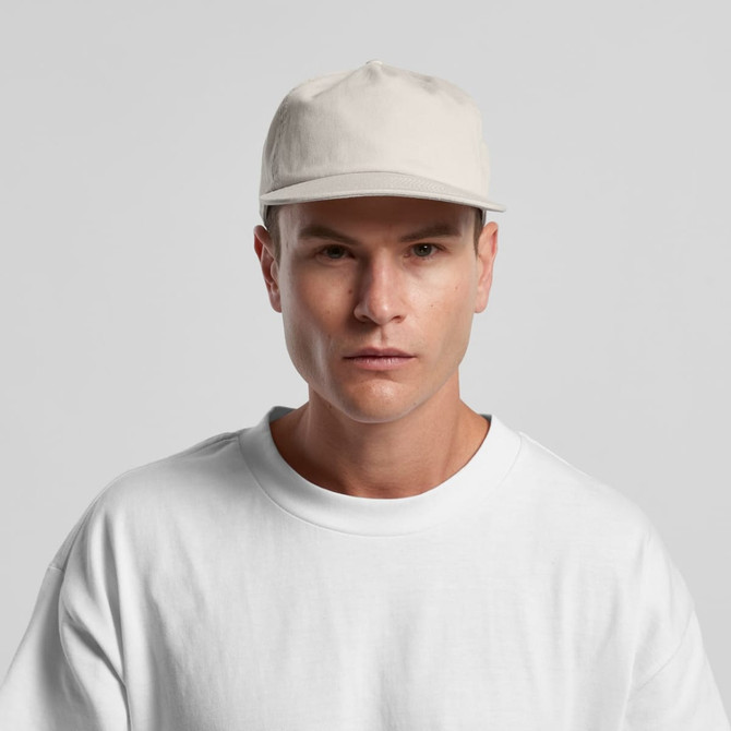 A light beige cap with a structured five-panel design, worn by a model in a plain white t-shirt.