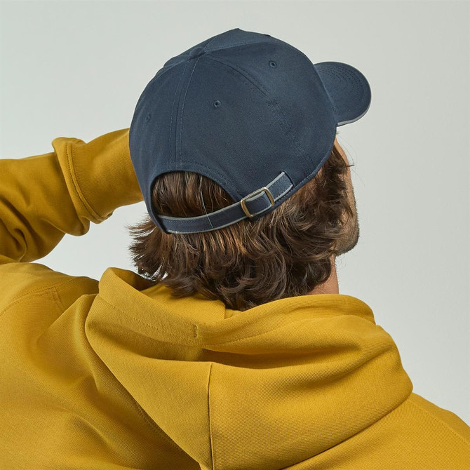 A navy cap with an adjustable strap, worn by a person in a yellow hoodie, viewed from the back.