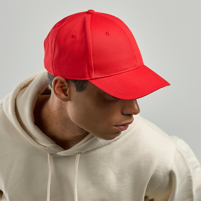 A red cap with a structured front and curved brim, worn by a person in a light-coloured hoodie.