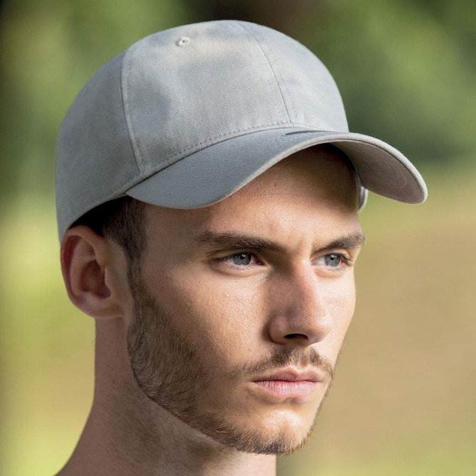 A grey cap with a curved brim, featuring a logo, worn by a model outdoors.