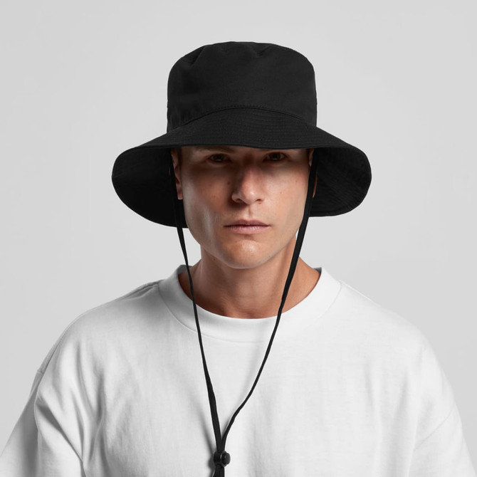 A black wide brim bucket hat with a chin strap, showcased on a model wearing a white sweatshirt.