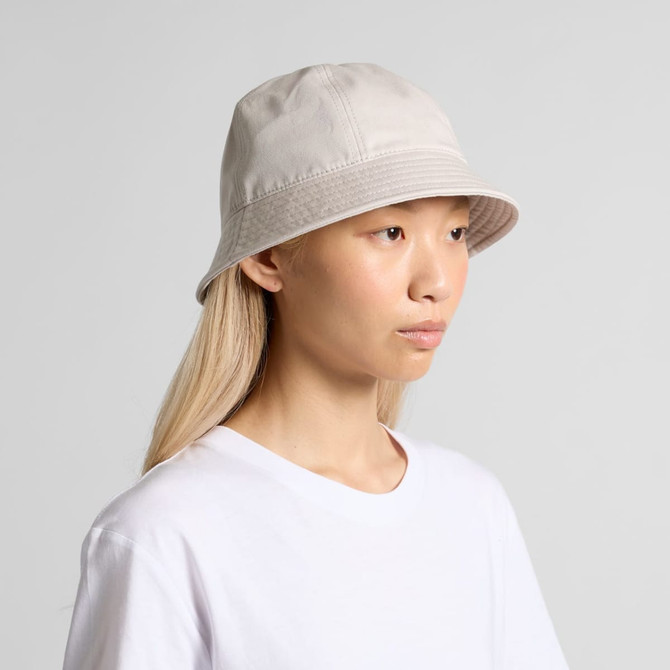 A light grey bucket hat sits on a model's head, featuring a simple design and a logo.