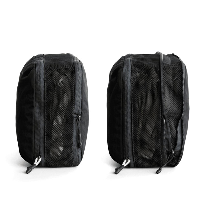 A black packing cube with mesh panels, featuring zip closures on both sides. It has a logo on one side.