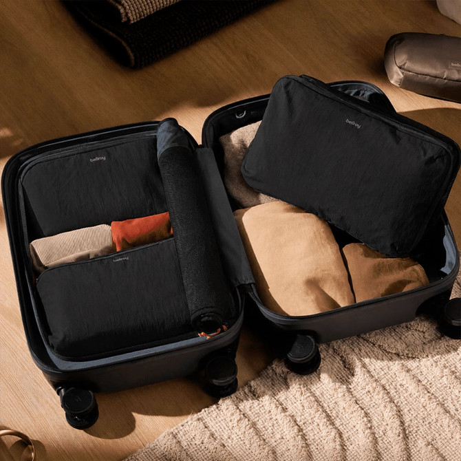 A black packing cube and a smaller pouch, both inside a suitcase, arranged with rolled and folded clothing.