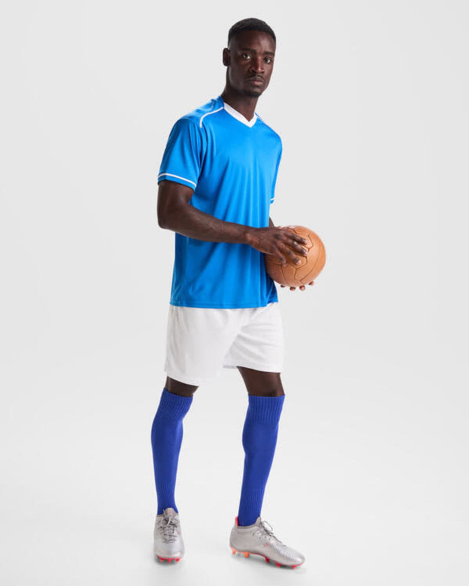 A male athlete wearing a blue sports jersey, white shorts, and blue knee-high socks, holding a brown sports ball.