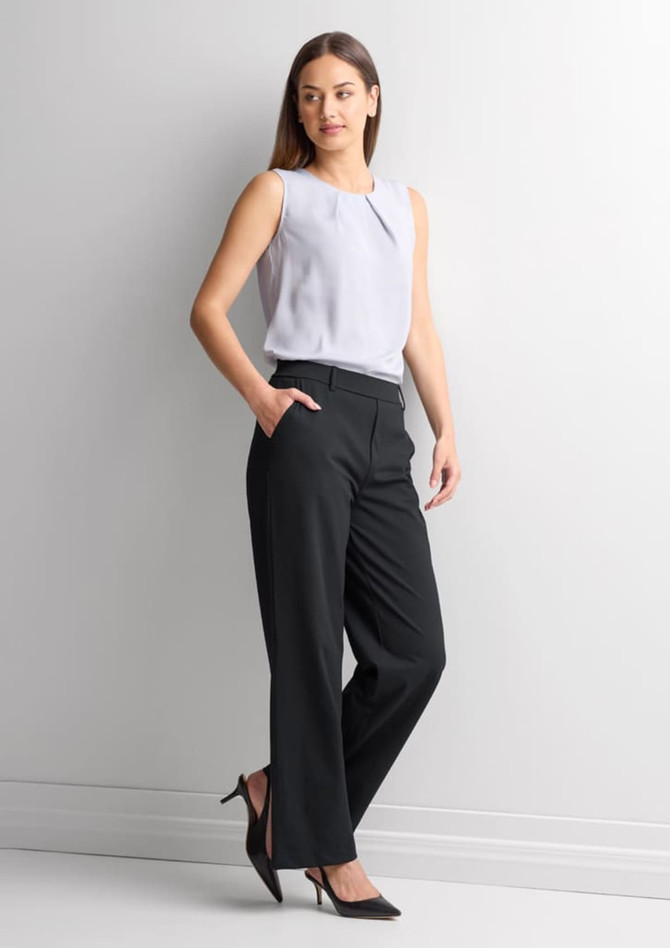 A woman stands wearing soft stretch pants in black, paired with a light grey sleeveless top and black heels.
