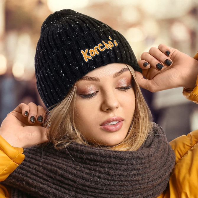 A black beanie with a textured pattern, worn by a person with a yellow jacket and grey scarf.