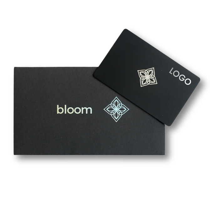 A black packaging box with a silver logo and a card featuring a design and the word "bloom."