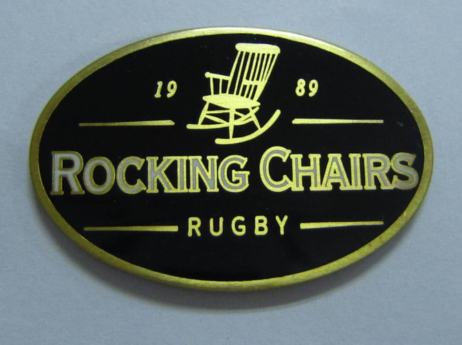 A black and gold hard enamel lapel pin featuring an illustration of a rocking chair with "Rocking Chairs Rugby" inscribed.