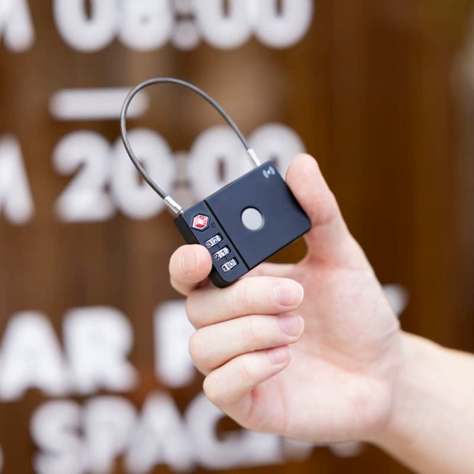 A black luggage lock with a keypad and a metal loop, held in a hand against a blurred background.