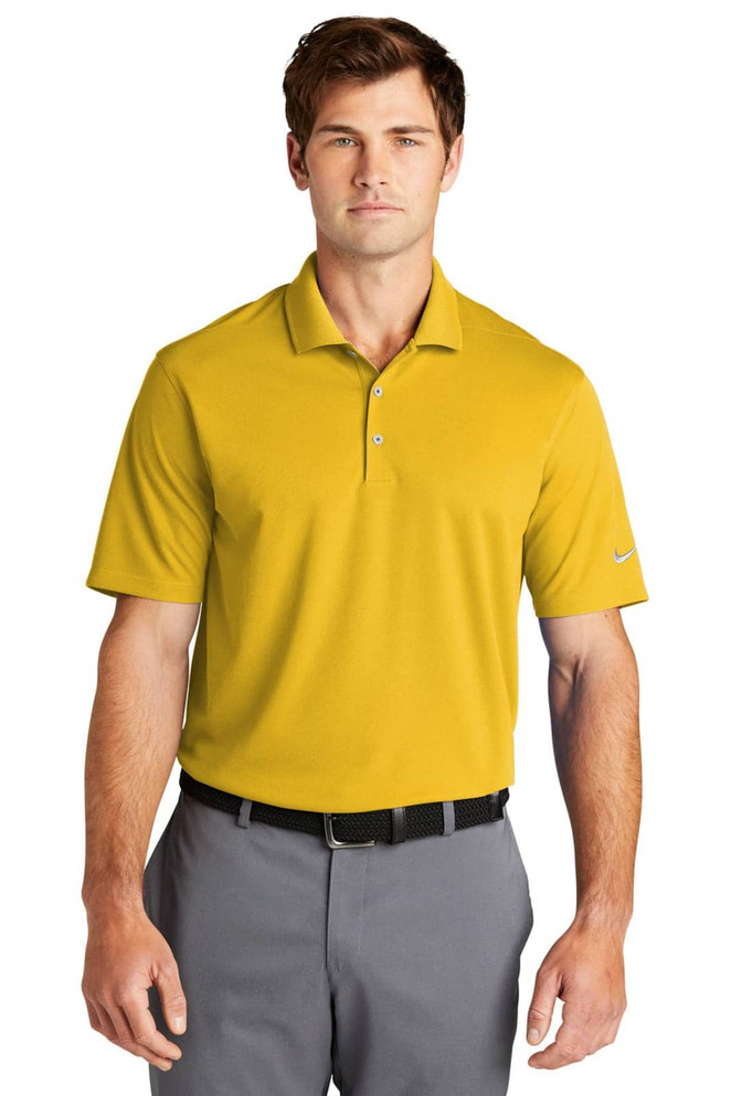 A man wearing a yellow polo shirt with a logo, styled with grey trousers and a belt.