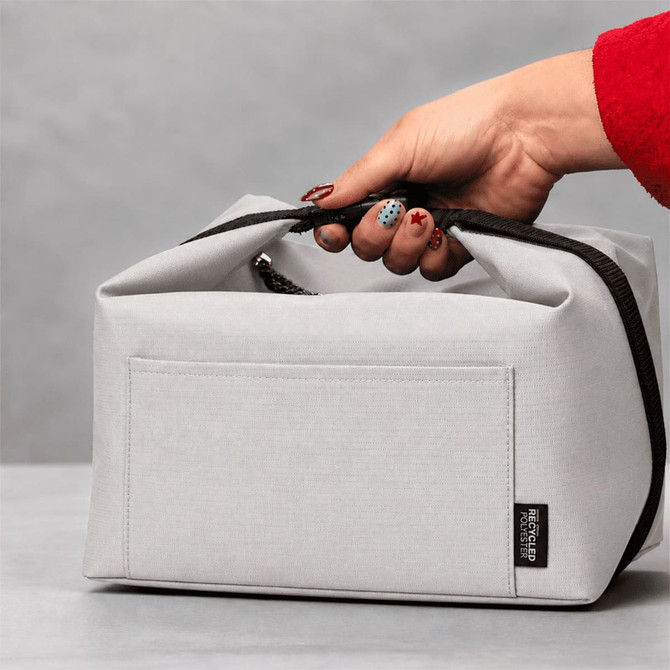 A grey recycled lunch cooler bag with a handle and a branded tag, being held by a hand.