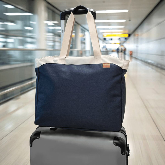 A navy blue tote bag with cream handles positioned on top of a suitcase in an airport setting.