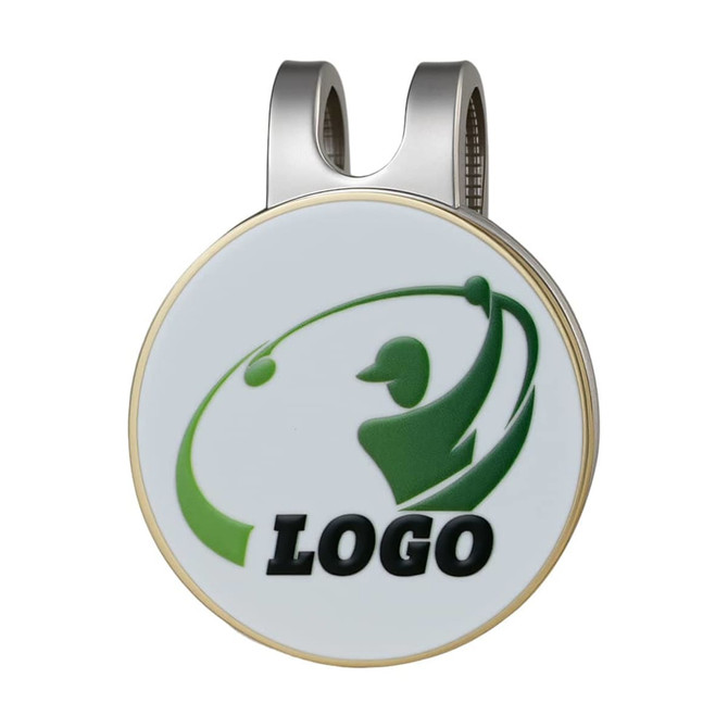 A round golf hat clip with a silver finish, featuring a logo and green graphic of a golfer.