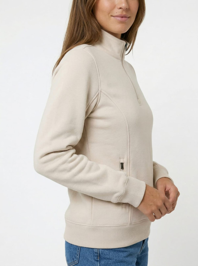 A woman wearing a beige half-zip fleece jumper with a side zipper and fitted cuffs. The jumper has a logo.