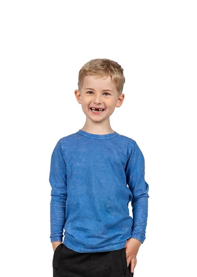 A boy smiles while wearing a long sleeve, stone wash T-shirt in blue. The shirt has a logo on it.