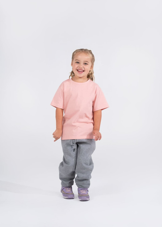 A smiling child wearing a pink T-shirt and grey sweatpants, standing against a plain white background.