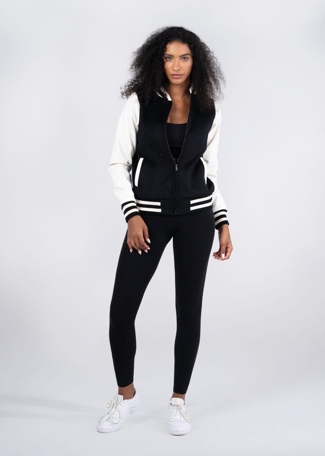 A women's wool blend varsity jacket in black and white, featuring a zip front and striped cuffs, alongside black leggings.