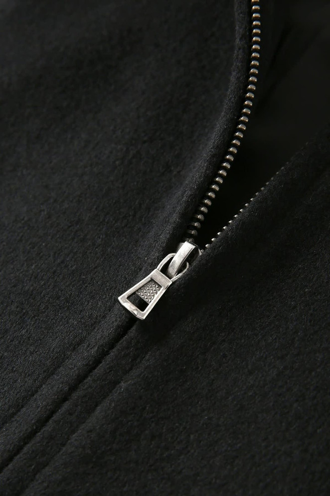 A close-up of a black wool blend varsity jacket featuring a silver zipper detail. The jacket has a logo.