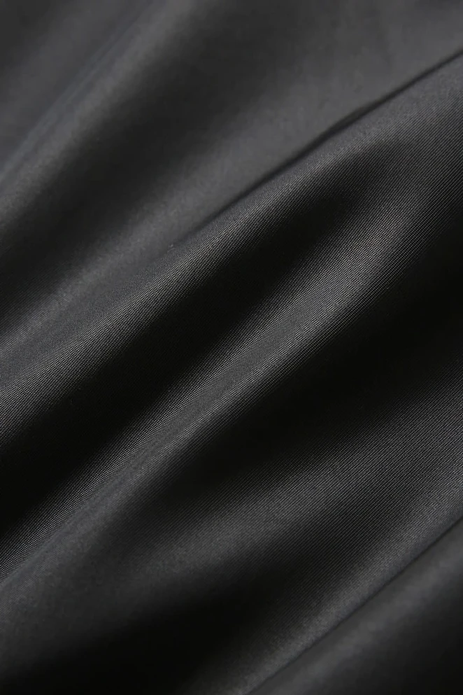 A close-up of smooth, black fabric showcasing soft texture and subtle sheen. The material appears fine and luxurious.