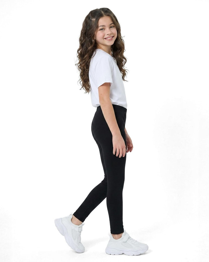 A pair of black kids' leggings worn by a girl wearing a white t-shirt and white sneakers, showcasing a side view.