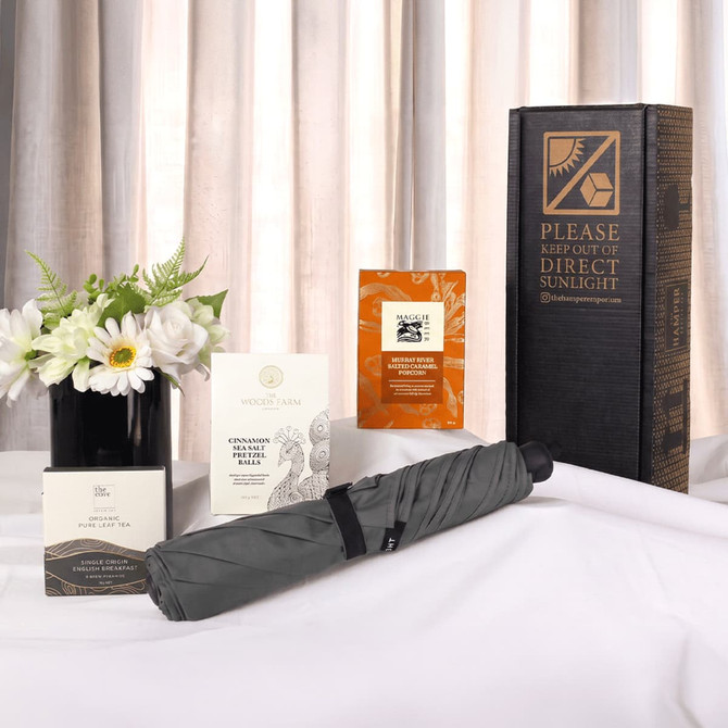 A grey umbrella, flower arrangement, and several boxes with a promotional package, all displayed on a white surface.