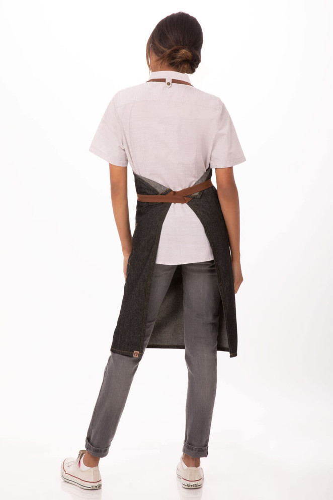 A person wearing a Memphis Bib Apron in dark grey, paired with a white shirt and grey jeans, showcasing a stylish workwear design.