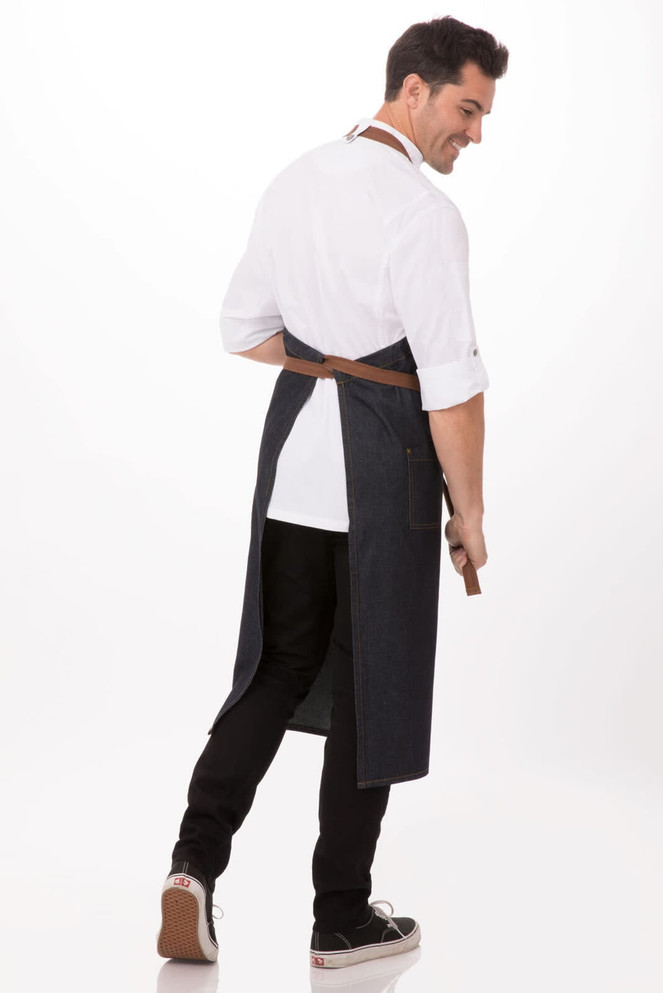 A dark denim bib apron with a brown belt, worn by a person turned slightly away from the camera.