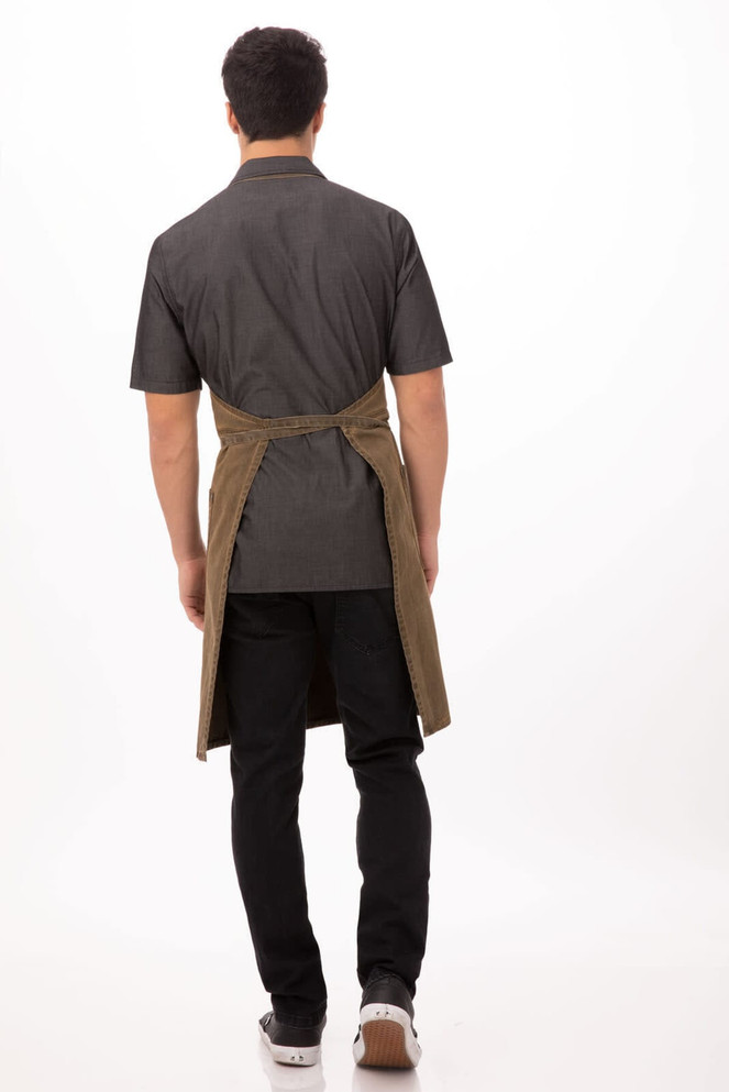 A dorset bib apron in dark grey with a contrasting brown tie, worn by a model from the back.
