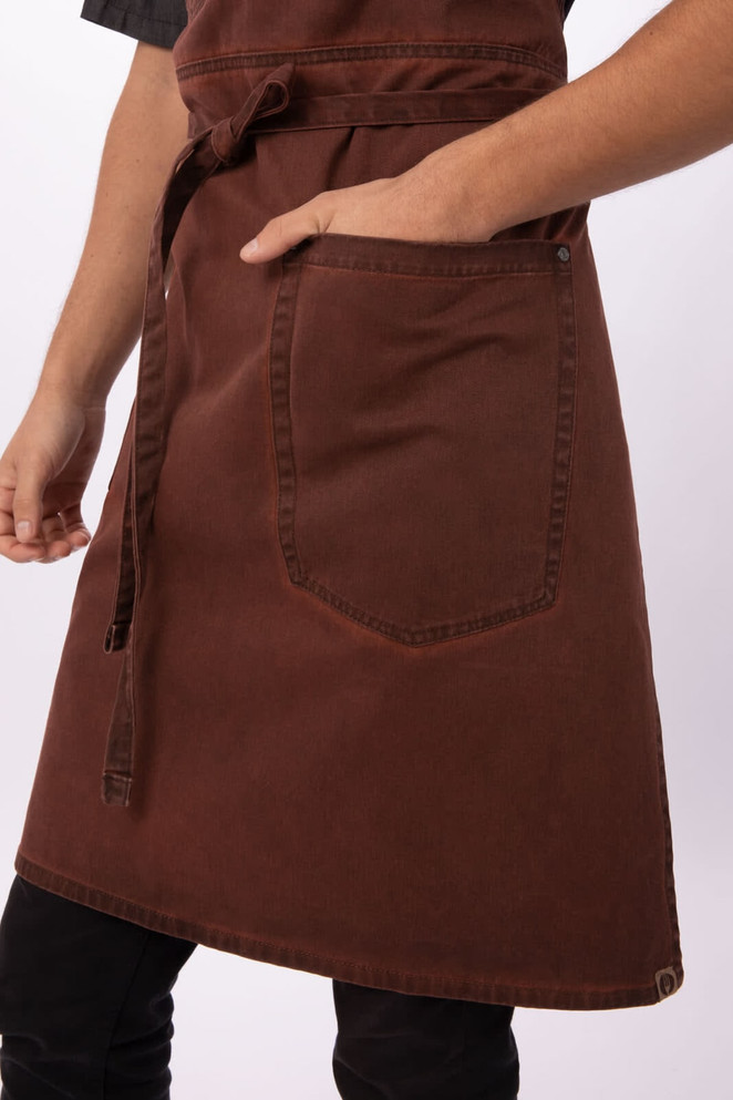 A brown Dorset bib apron with a front pocket, featuring a tied waist and sturdy fabric.