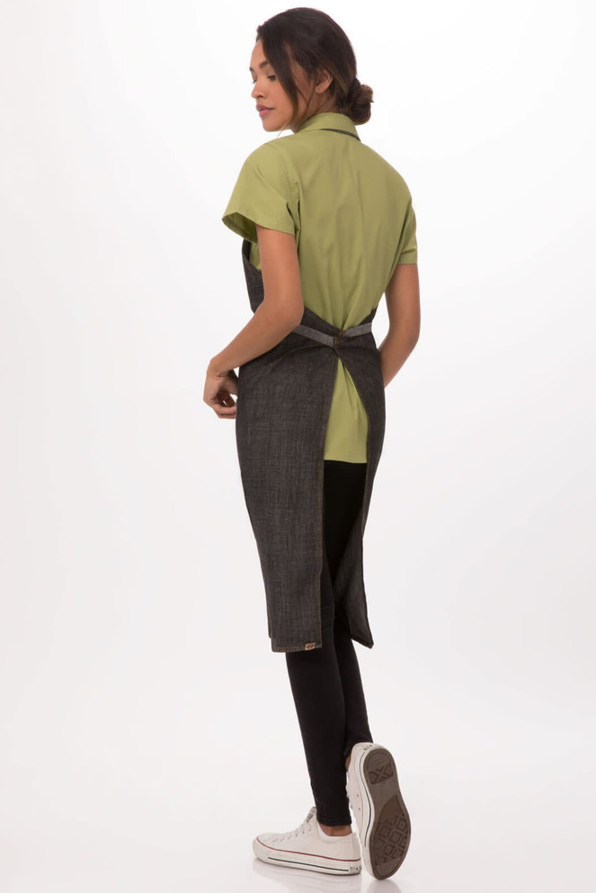 A woman wearing a green shirt and a black Manhattan Bib Apron from the back, featuring a tied waist.